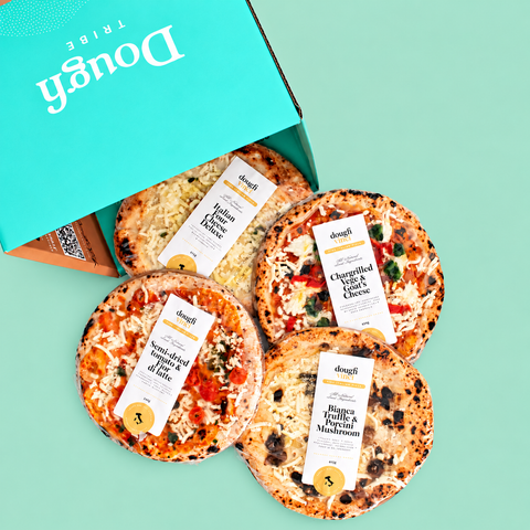 Four artisanal pizzas arranged in front of an open turquoise box labeled Dough Tribe on a mint green background. The pizzas have visible labels for flavors including Pepperoni & Jalapeño, Chicken & Cheese, and Bianca Guacfulful Mushroom.