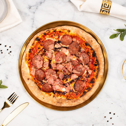 Cooked Doughvinci Meatlovers pizza topped with salami, ham, tomato sauce and melted cheese on a blistered woodfired sourdough crust, served on a gold tray on white marble with gold cutlery and a linen napkin