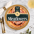 Doughvinci Meatlovers pizza in retail packaging, a handstretched sourdough base woodfired in Italy and topped in Australia, displayed on a gold beaded platter with gold cutlery, a linen napkin and a glass of white wine on white marble